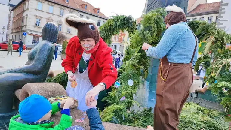 Zwei mannsgroße Osterhasen nehmen am Brunnen Basteleien der Kinder entgegen. © Stadt Schmölln